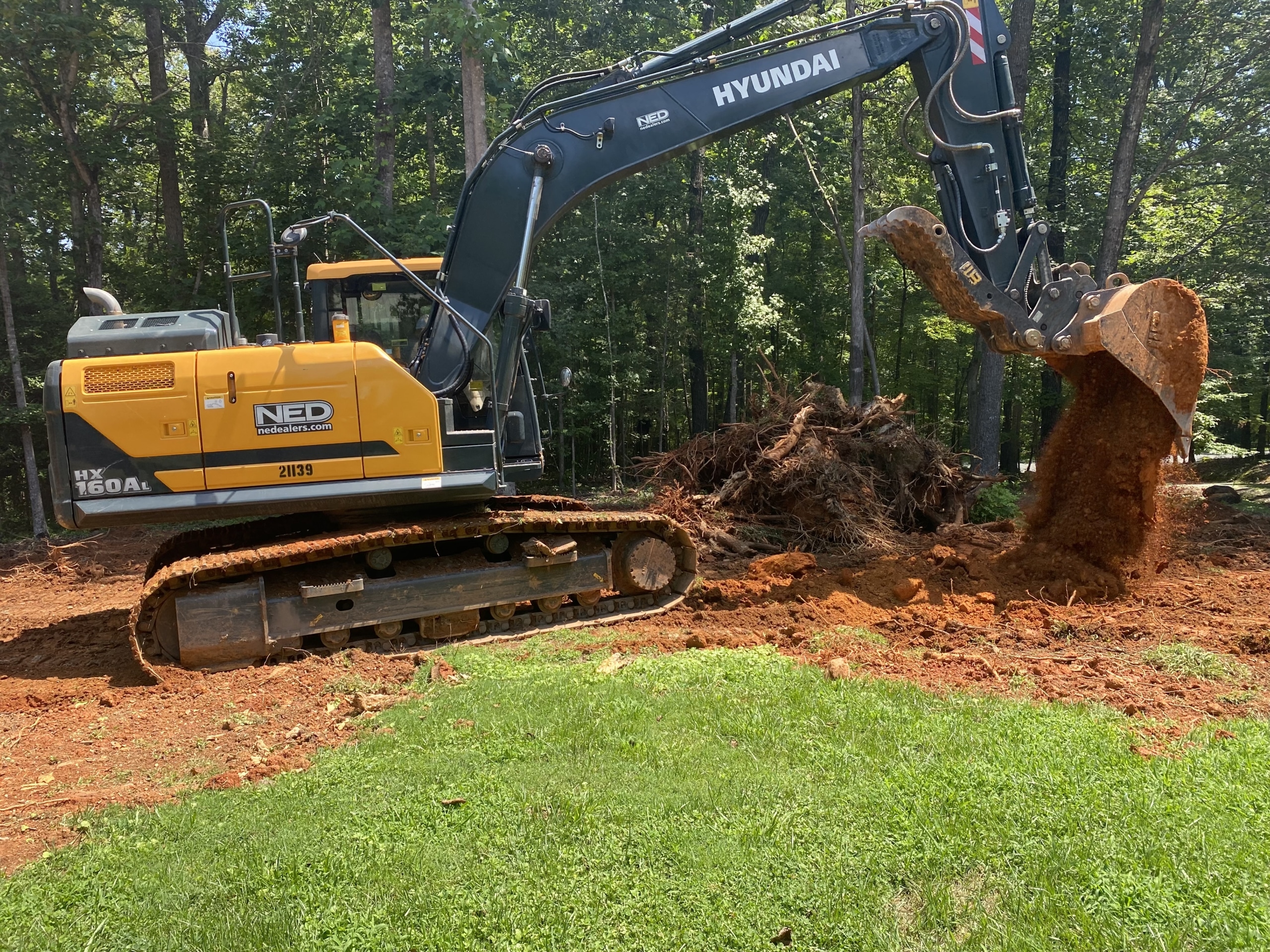 Hyundai HX160A excavator digging into the ground with a bucket attachment.