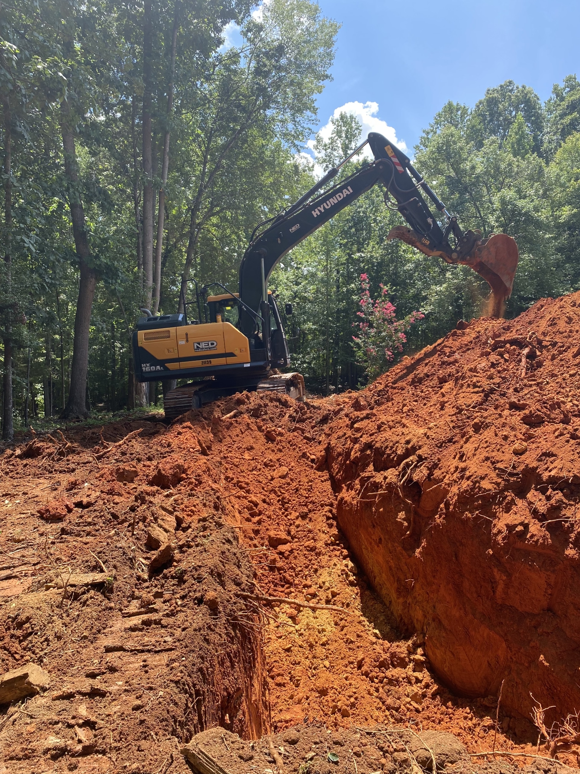 A yellow Hyundai excavator digging into a mound of reddish soil at a construction site.