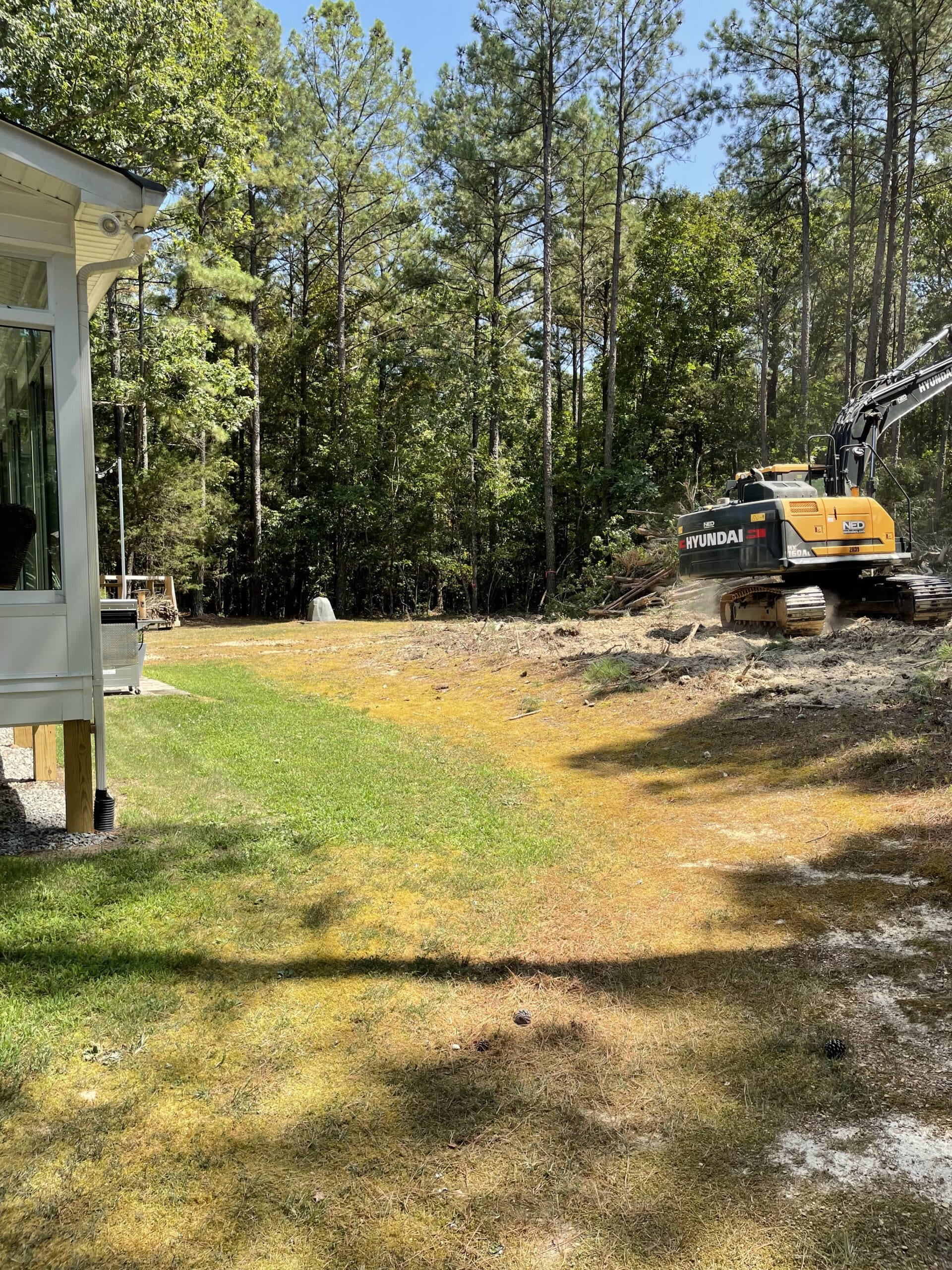 A Hyundai excavator working on a construction site surrounded by trees and grass.