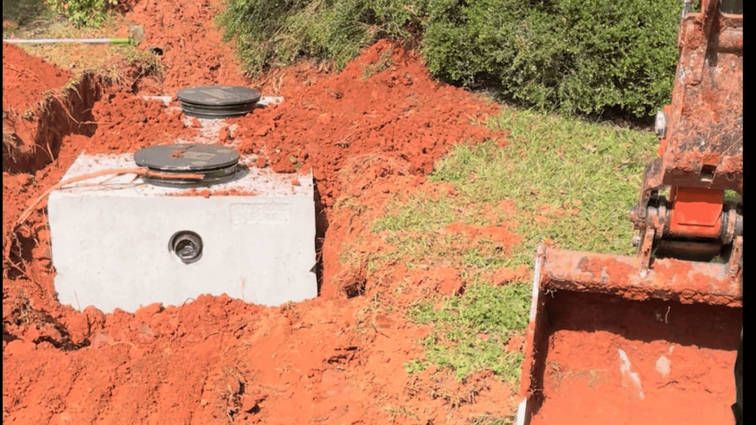 Septic tank partially buried in red soil with two access covers visible.