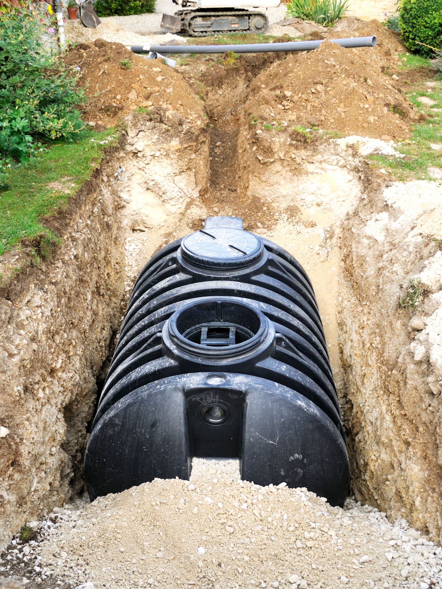 Black septic tank positioned in an excavated trench with surrounding earth.