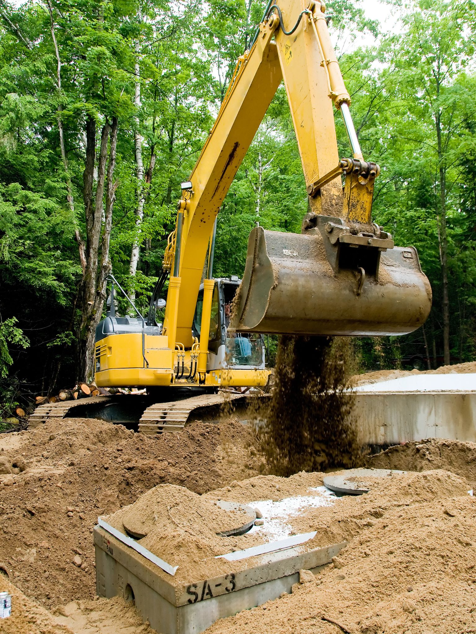 Yellow excavator operating on a construction site, moving dirt and sand from a pile.